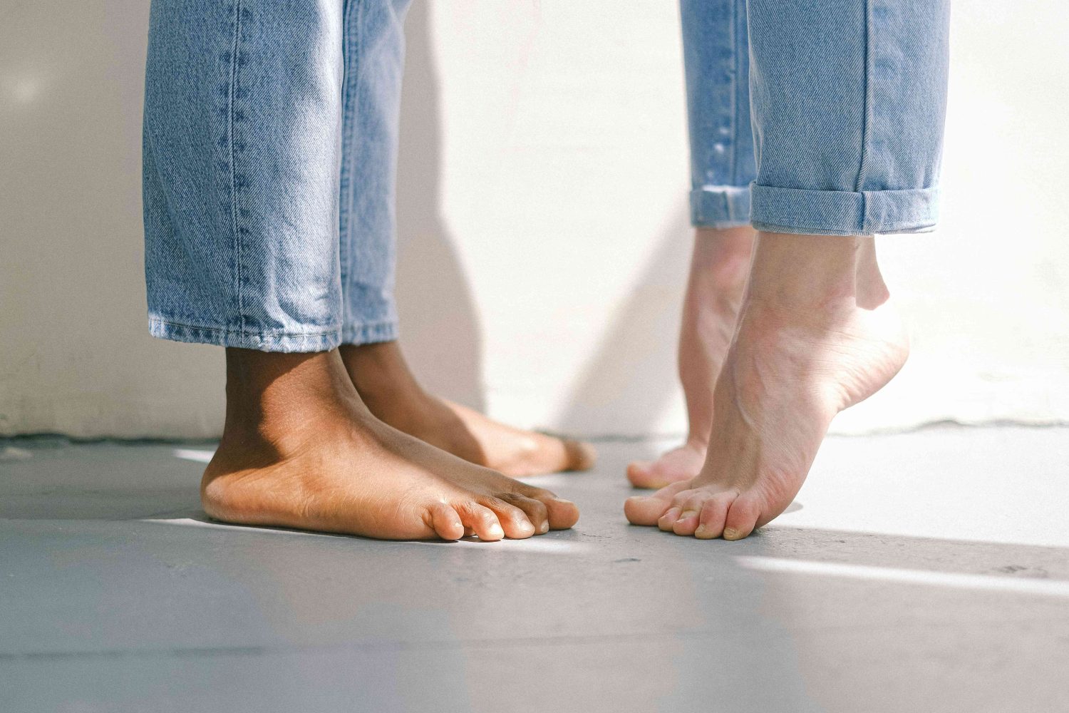 Close-up of two pairs of bare feet, one standing flat and the other raised on toes, showing healthy skin and varying skin tones—used to illustrate typical foot posture and skin condition before the appearance of blisters, calluses, or ulcers